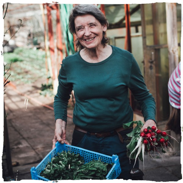Eine freundliche Mitarbeiterin in der Gartenwerkstatt mit einer Gemüsekiste und Radieschen in der Hand