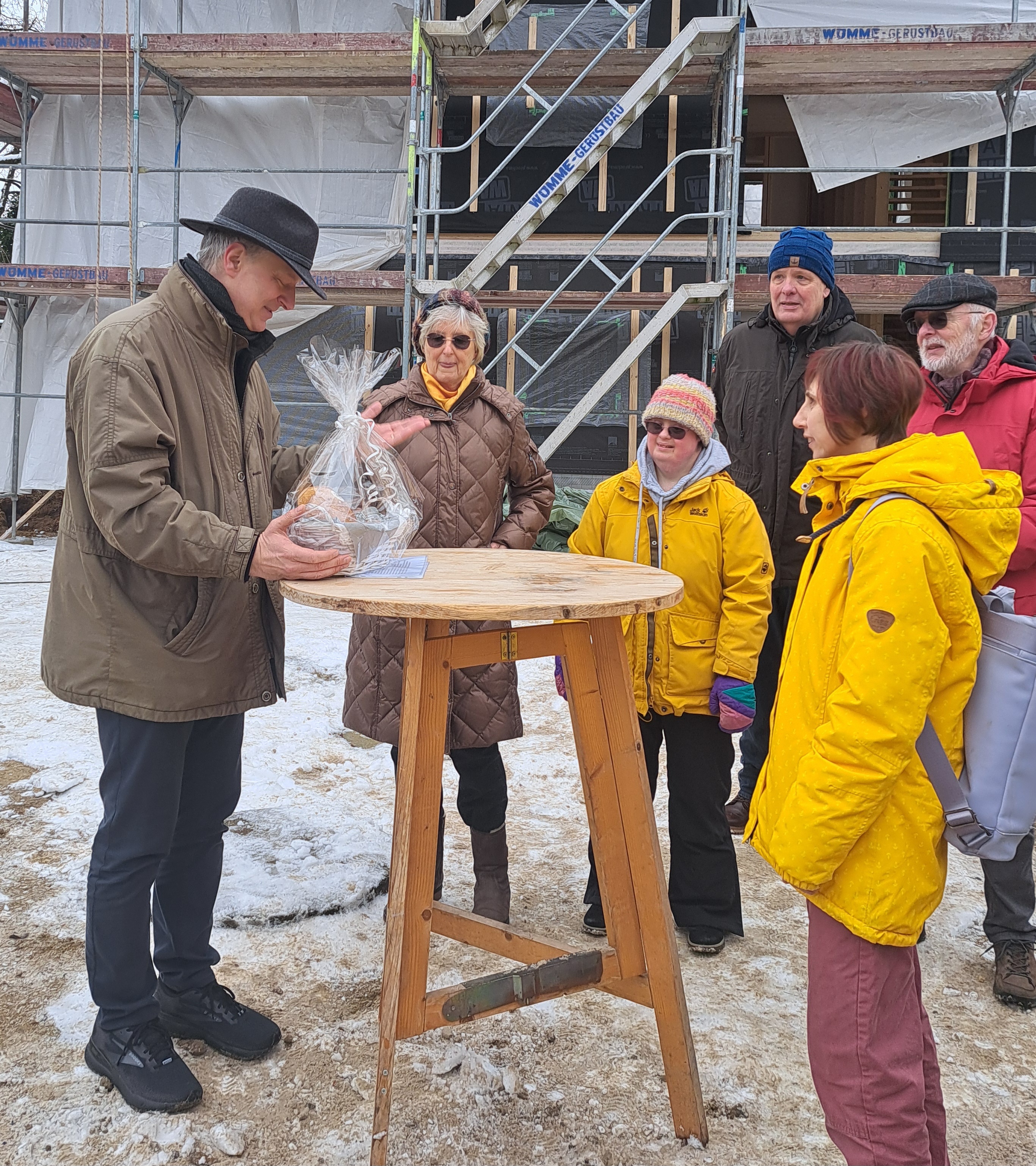 Richtfest des Bauprojektes in Quelkhorn mit Geschenkübergabe des Bürgermeisters an Bewohner*innen anlässlich des Richtfestes. Im Hntergrund die Baustelle.